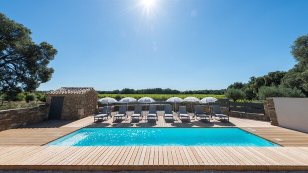 Un terrazzo in legno con piscina, poltrona a sdraio e ombrelloni.
