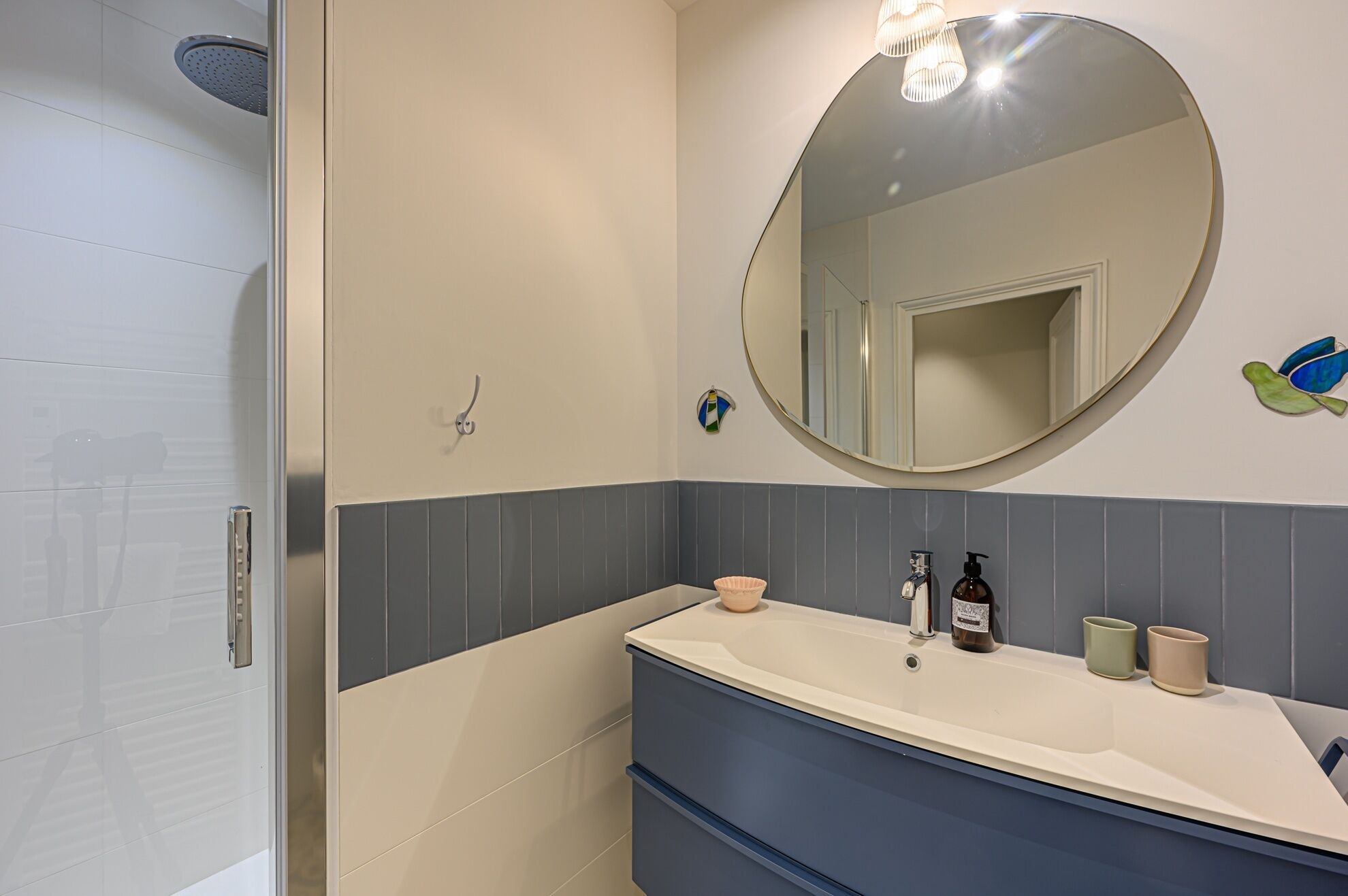 Une salle de bain avec un mur recouvert de carreaux blancs et bleus, un miroir rond, un lavabo avec deux bouteilles de savon et un porte-serviettes.