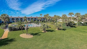 A resort with a pool, palm trees, and a building with arched windows. - Modern St Augustine Beach Condo with Pool and Private Garage, Steps to Ocean. (St. Augustine)