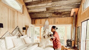 Ein rustikales Schlafzimmer mit einem großen Bett, Holzwänden, einem Oberlicht und einem Kamin.