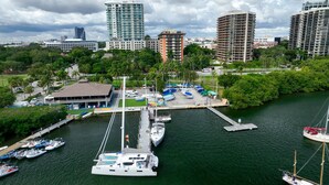 Un port de plaisance où sont amarrés différents types de bateaux, entouré d’une végétation luxuriante et avec des bâtiments modernes en arrière-plan.