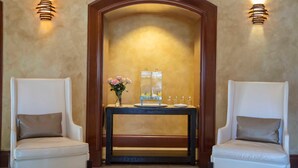 A room with two white leather chairs, a wooden console table with a vase of flowers, and wall sconces. - Bayfront Condo: Coconut Grove & Pool Access (Miami)