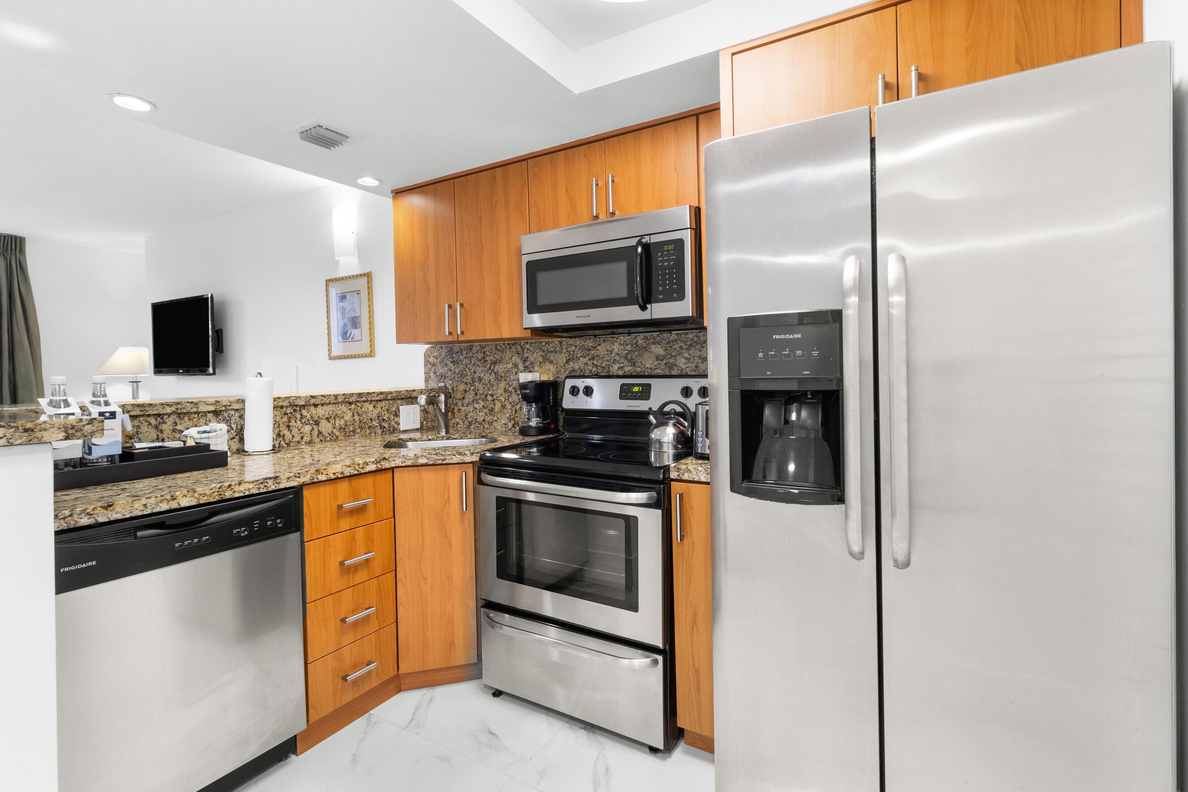 A modern kitchen with stainless steel appliances, wooden cabinets, granite countertops, and a built-in dishwasher.