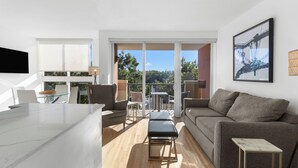 Un salon moderne avec un canapé, une table basse et un banc. Il y a également un coin cuisine avec des placards et une table à manger. La pièce est dotée de grandes fenêtres et offre une vue sur l’extérieur.