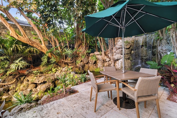 A patio with a table and chairs, surrounded by tropical plants and a small waterfall.