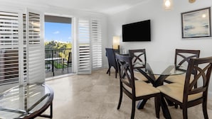Un coin repas avec une table et des chaises en verre, un téléviseur fixé au mur et un tableau accroché au mur.