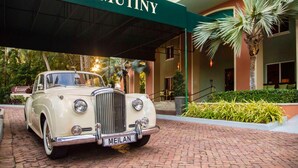 Un coche antiguo estacionado frente al hotel The Mutiny, con un camino de ladrillo y palmeras.