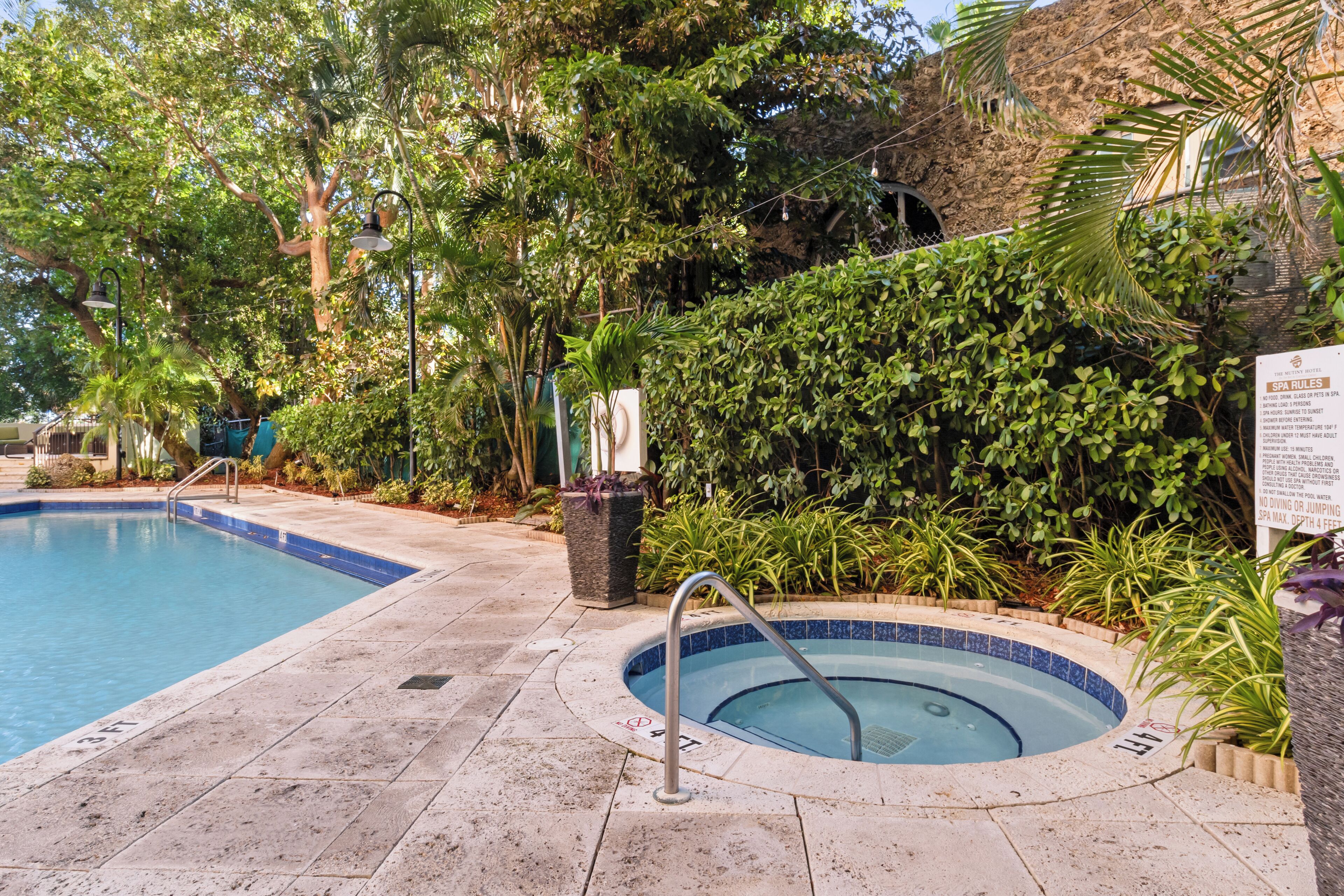 A swimming pool with a hot tub, surrounded by lush greenery and a sign with spa rules.