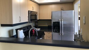 Une cuisine moderne avec des meubles de couleur bois clair, des appareils en acier inoxydable, un plan de travail noir et une lucarne au-dessus de l’évier.