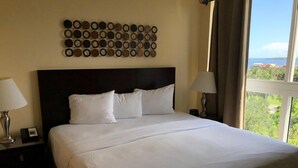 Une chambre d’hôtel avec un grand lit, deux lampes de chevet, un élément décoratif circulaire fixé au mur, et une vue sur la verdure et les bâtiments par la fenêtre.