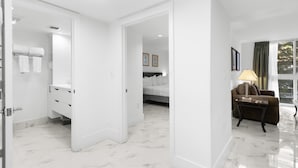 A hotel room with a bathroom, a bed, a sofa, and a view of trees through the window.