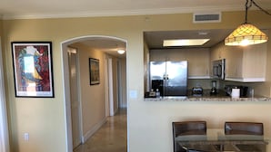 A kitchen with a stainless steel refrigerator, microwave, and coffee maker. There is a dining table with chairs and a hanging light fixture. - Family Retreat, 2 Bedroom Condo, Pool Access (Miami)