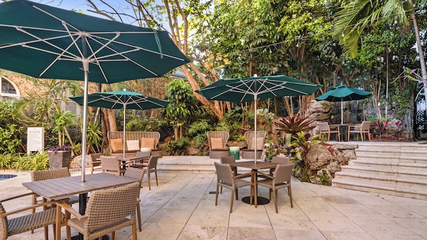An outdoor patio area with wicker furniture, green umbrellas, and a stone floor. - Family Retreat, 2 Bedroom Condo, Pool Access (Miami)