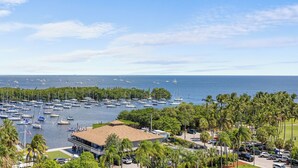 A marina with numerous boats, a building with a flat roof, and a parking area with cars. - Luxury 2/2 Condo with balcony in Coconut Grove (Miami)