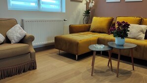 Un salon avec un canapé de couleur moutarde, un fauteuil plus petit et une petite table sur laquelle est posée une plante en pot.