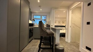 A modern kitchen with a central island, a dining area with a bar, and a bedroom visible through an open door. - House - Sleeps 4 & Free Parking (London)