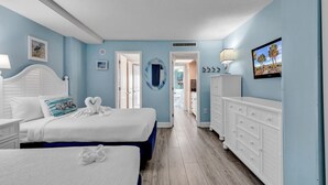 Une chambre avec deux lits, une commode et un téléviseur. Un couloir mène à une autre pièce.