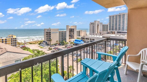 Un balcon avec des chaises turquoise donnant sur une plage et offrant une vue sur la ville.