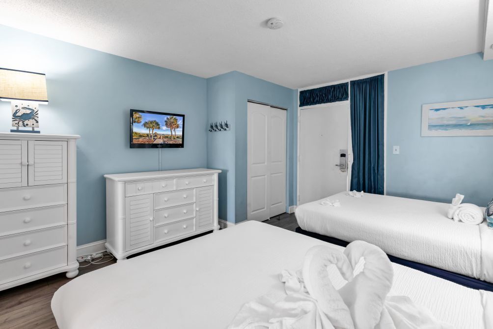 A hotel room with two beds, a white dresser, a television, and a door.