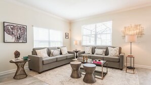 A living room with a grey sofa, two coffee tables, a rug, and a painting on the wall. - Last Minute Disney Getaway! Townhouse with Private Pool. Book Now! #118113 (Orlando)