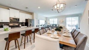 A modern kitchen with white cabinets, a central island, and a dining area with a long table and chairs. - Last Minute Disney Getaway! Townhouse with Private Pool. Book Now! #118113 (Orlando)