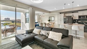A modern living room with a sectional sofa, a dining area with a table and chairs, a kitchen with a bar, and a large sliding glass door leading to an outdoor patio. - Last Minute Disney Getaway! Luxury Condo with Private Balcony. Book Now! #65877 (Orlando)