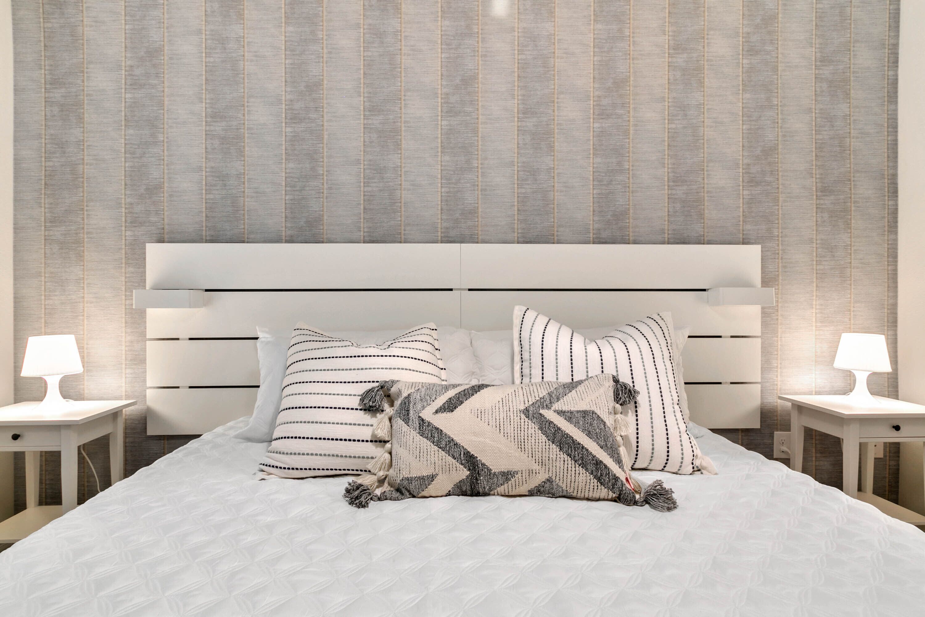 A neatly made bed with striped and chevron-patterned pillows, a white headboard, and bedside tables with lamps.