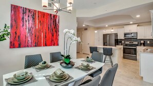 A modern dining area with a white table set for six, surrounded by grey chairs. A red abstract painting adorns the wall above the table. - Last Minute Disney Getaway! Luxury Condo with Private Balcony. Book Now! #66025 (Orlando)