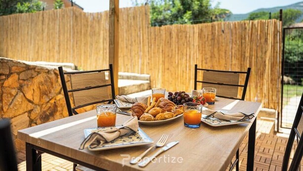 Un espacio exterior para comer con una mesa de madera preparada para el desayuno, que incluye croissants, uvas y jugo de naranja.