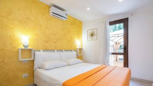 Un dormitorio con cama, dos lámparas de noche, aire acondicionado, ventana con cortinas y vistas al exterior.