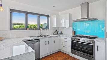 A modern kitchen with white cabinets, a stainless steel stove, and a large window overlooking greenery.