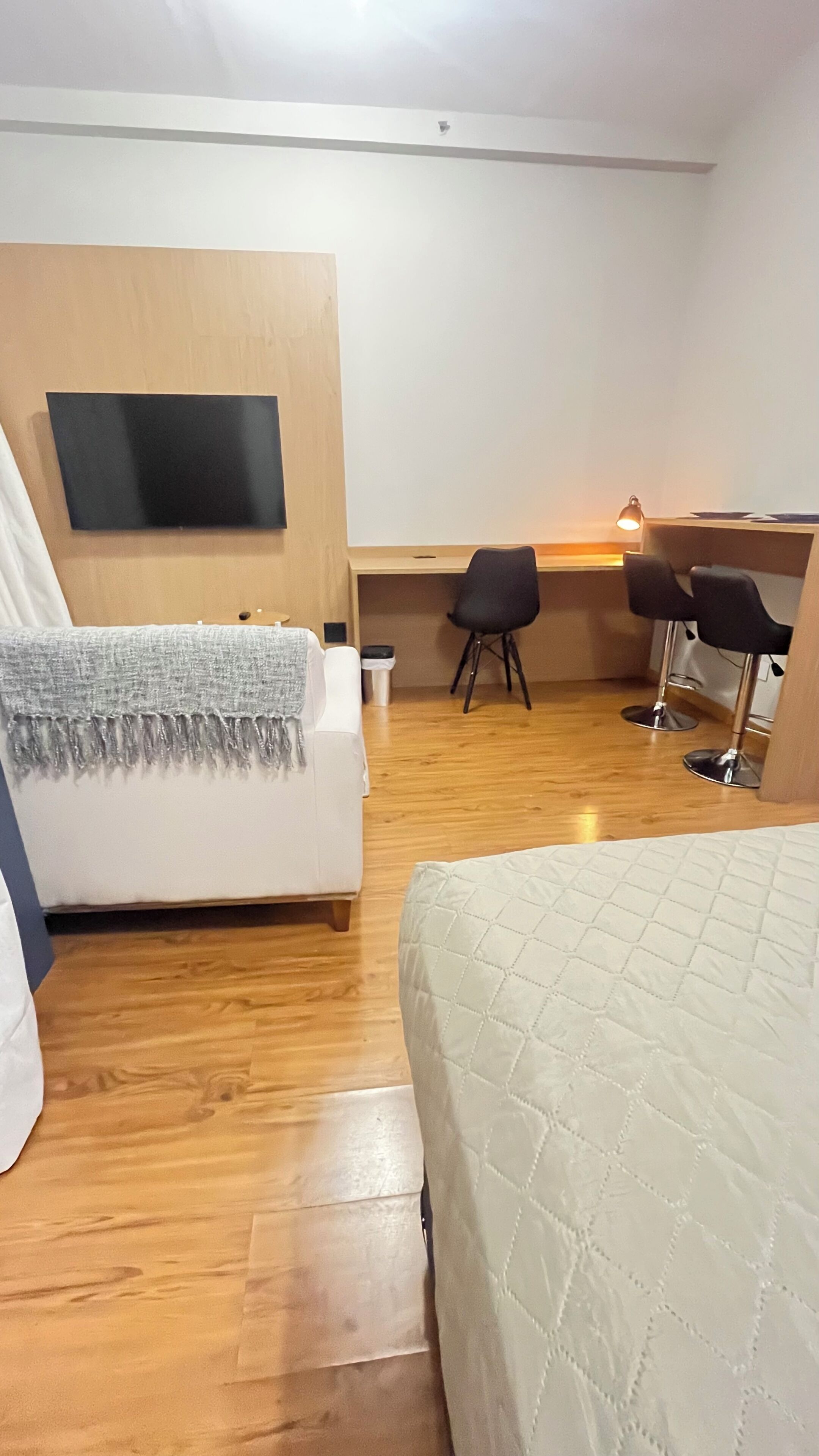 Una camera d'albergo con un letto, una scrivania con due sedie, una TV a muro e un pavimento in legno.