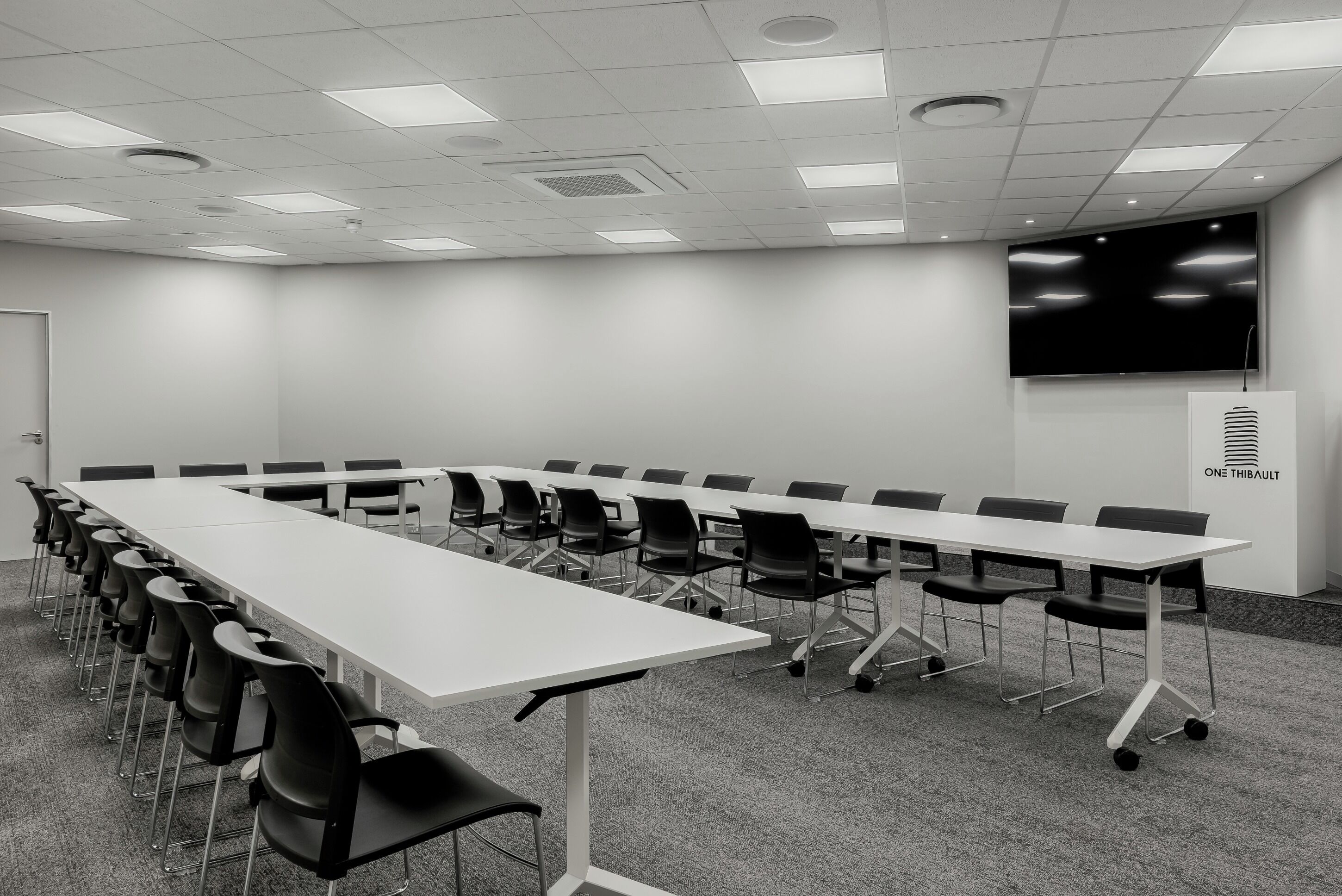A conference room with a long table, chairs, a projector screen, and a ventilation unit.