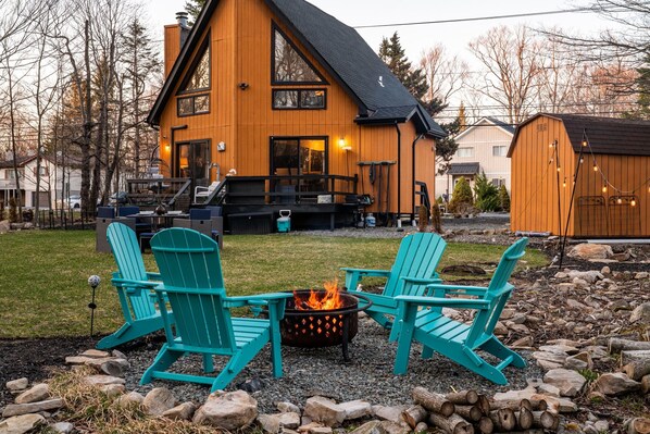 A modern wooden house with a large deck, a fire pit, and two turquoise Adirondack chairs. - Pet Friendly, Pocono Chalet, Lake Community (Tobyhanna)