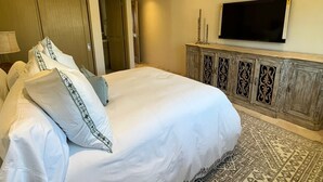 Een slaapkamer met een groot bed, een plafondventilator, een flatscreen-televisie en een kamerkleed met een patroon.