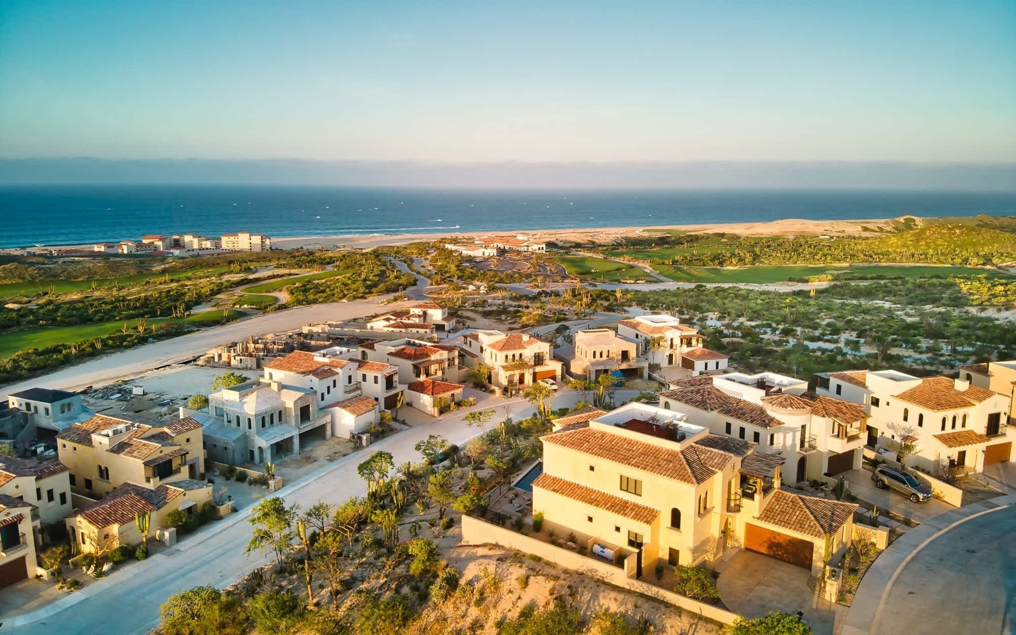 Zona residencial costeira com casas de arquitetura mediterrânea, uma estrada e vista para o oceano.