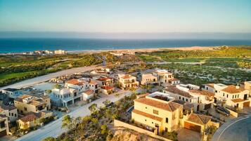 A coastal residential area with houses featuring Mediterranean architecture, a road, and a view of the ocean.