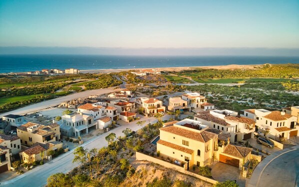 A coastal residential area with houses featuring Mediterranean architecture, a road, and a view of the ocean.
