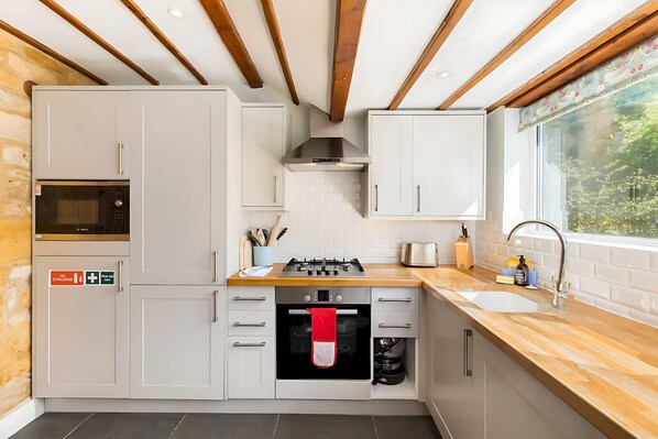 A modern kitchen with white cabinets, a built-in oven, a gas stove, and a window with a view of greenery. - *NEW* Moreton Cottage | Central | Garden - Pass the Keys (Moreton-in-Marsh)
