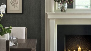 A dining area with a fireplace, framed botanical prints, and a vase with flowers.