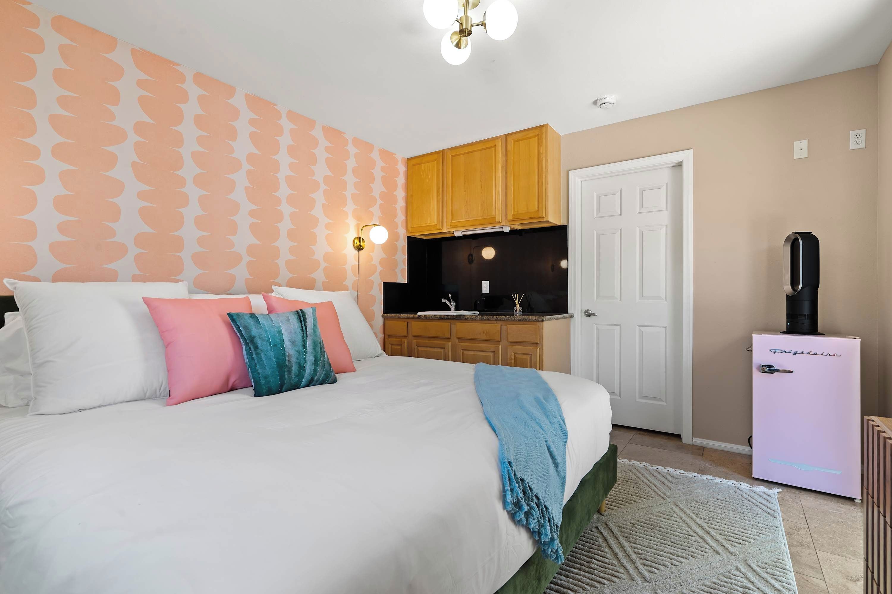 A bedroom with a bed, pillows, a bedside table, a nightstand, a wall-mounted light, a ceiling fan, and a window.