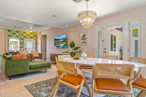 A modern living room with a green sofa, wooden chairs, a round dining table, and a chandelier.