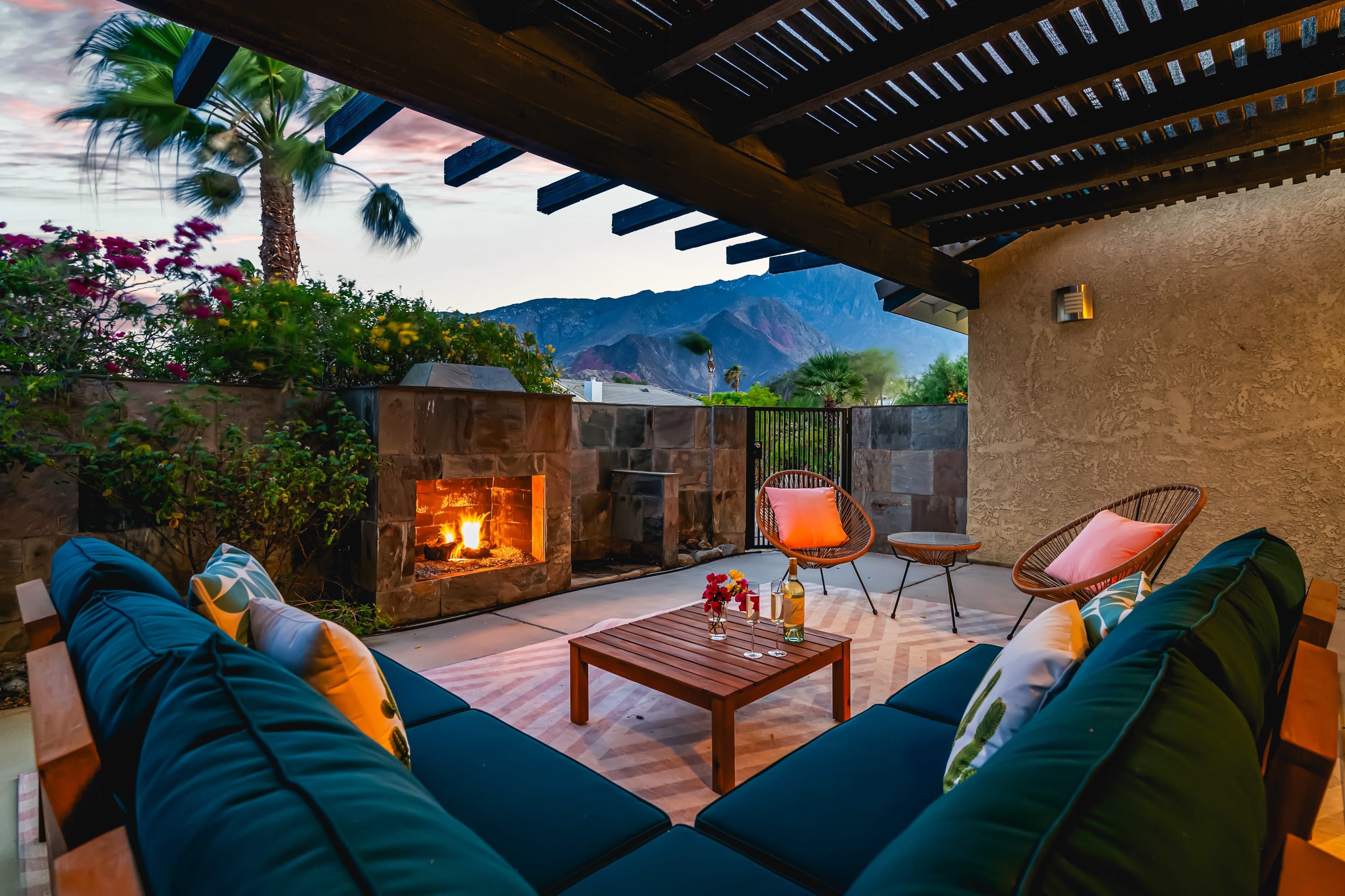 A cozy outdoor seating area with a fire pit, cushioned seating, and a pergola overhead.