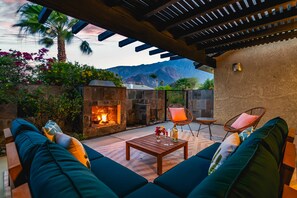 A cozy outdoor seating area with a fire pit, cushioned seating, and a pergola overhead.