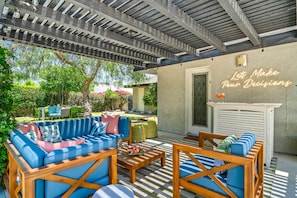 An outdoor patio area with a blue sofa set, wooden chairs, and a white bar area.