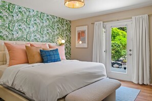 A bedroom with a bed, a door leading to an outdoor area, and a wall with a leafy pattern.