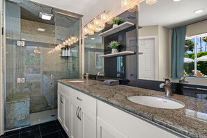 A modern bathroom with a glass-enclosed shower, granite countertops, and a large mirror with integrated lighting.