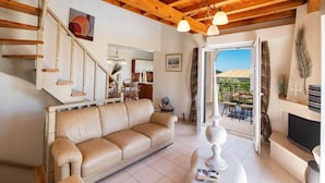 Un salon chaleureux avec un canapé beige, un escalier et une vue sur l’extérieur.