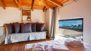 Une chambre avec un plafond en bois, un canapé-lit, une fenêtre donnant sur un paysage et un lit avec des serviettes.