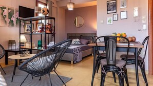 Ein modernes Wohnzimmer mit einer Couch, einem Esstisch mit Stühlen, einem Bücherregal und einem Fernseher.